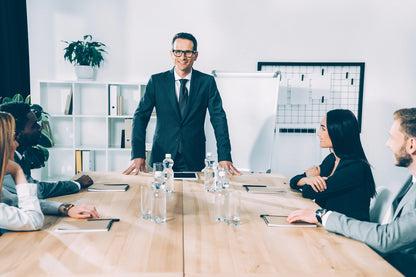 Man in a suit standing at a conference table with colleagues in an office setting
