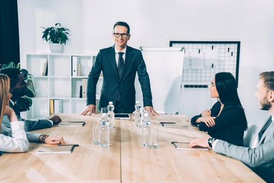 Man in a suit standing at a conference table with colleagues in an office setting