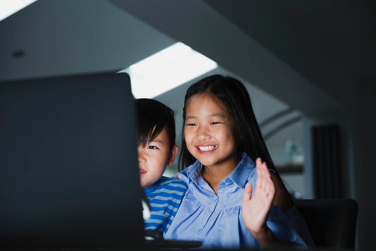 Two children sitting together, looking at a laptop screen with a dark background.